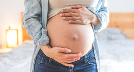 Caucasian pregnant mother touching her naked tummy, blue jeans, close upの写真素材