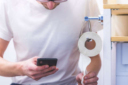Close up of young man using his smartphone while sitting on the toiletの写真素材