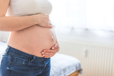 Caucasian pregnant mother touching her naked tummy, blue jeans, close upの写真素材
