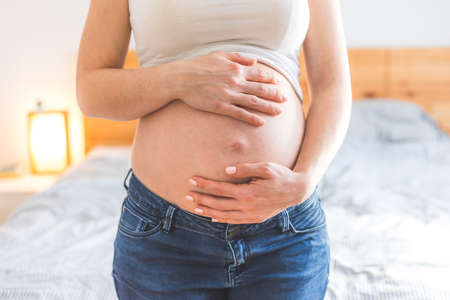 Caucasian pregnant mother touching her naked tummy, blue jeans, close upの写真素材