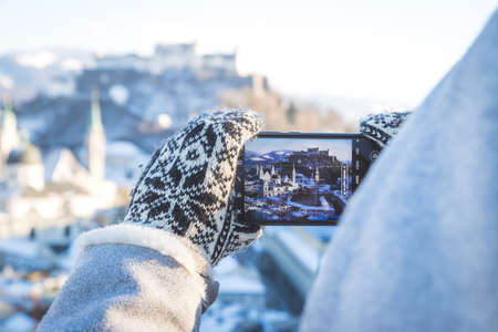 Young tourist woman is making a photo of Salzburg with her smartphone, winter timeの写真素材