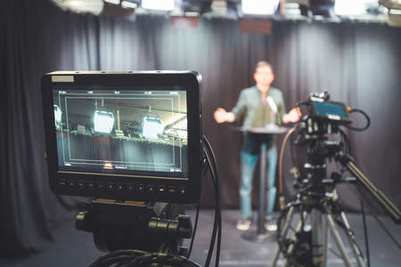Male journalist in a television studio talks into a microphone, film camerasの写真素材