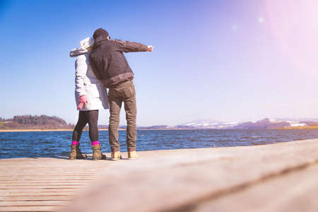 Young couple is standing on a footbridge and enjoys the view over the lake, winter timeの写真素材
