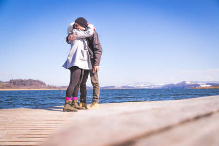 Young couple is standing on a footbridge and enjoys the view over the lake, winter timeの写真素材
