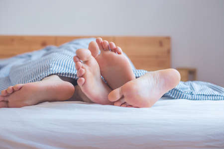 Close up a couples uncovered feet sleeping in bed, morningの写真素材