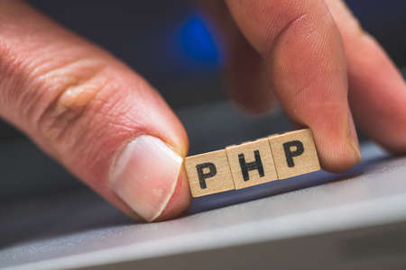 Wooden cubes with the letters âPHPâ are lying on a laptopの写真素材