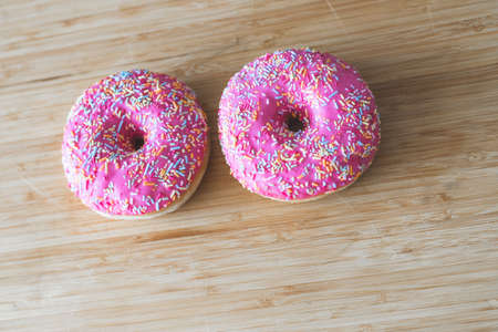Sugar sprinkled pink donut on wooden plateの写真素材