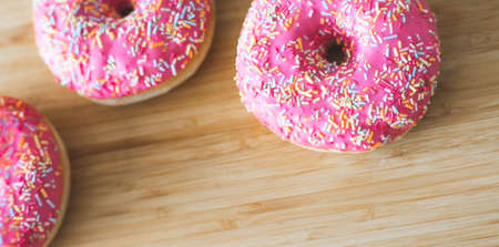 Sugar sprinkled pink donut on wooden plateの写真素材