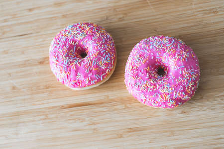 Sugar sprinkled pink donut on wooden plateの写真素材