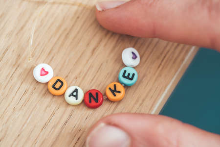 Close up of hand holding a bracelet made out of letters with the word â€œDankeâ€, close up