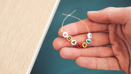 Close up of hand holding a bracelet made out of letters with the word âDankeâ, close upの写真素材