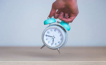 Male hand is holding a retro styled white alarm clock, isolatedの写真素材