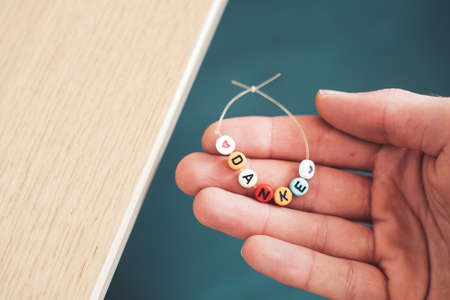 Close up of hand holding a bracelet made out of letters with the word âDankeâ, close upの写真素材