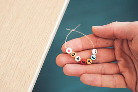 Close up of hand holding a bracelet made out of letters with the word âDankeâ, close upの写真素材