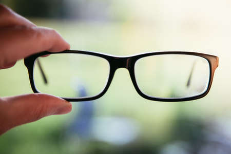 Young man holding his glasses outdoors, blurry backgroundの写真素材
