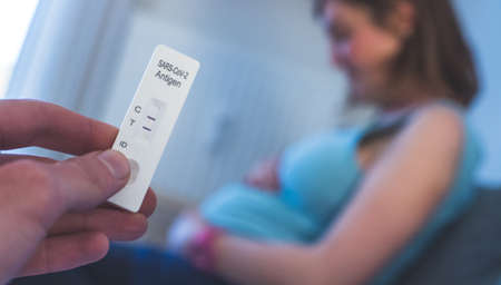 Close up of fingers holding express antigen covid test, positive result. Pregnant woman in the blurry backgroundの写真素材
