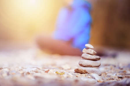 Cairn on a pebble beach, meditating woman in the background. Morning sun.の写真素材