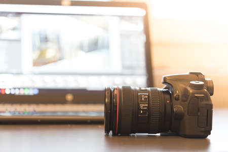 Professional camera with telephoto lens on a table, laptop in the blurry backgroundの写真素材