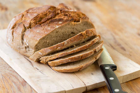 Fresh dark bread in slices. Wooden cutting board and table, knife.の写真素材