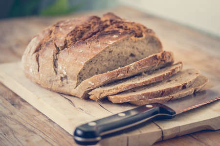 Fresh dark bread in slices. Wooden cutting board and table, knife.の写真素材