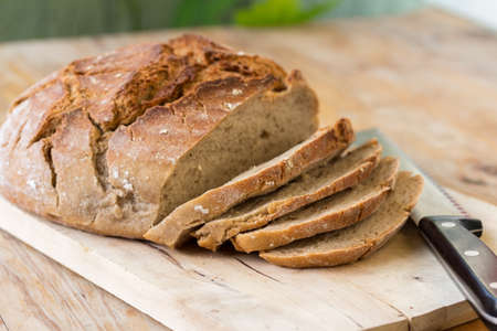 Fresh dark bread in slices. Wooden cutting board and table, knife.の写真素材