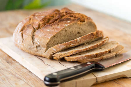 Fresh dark bread in slices. Wooden cutting board and table, knife.の写真素材