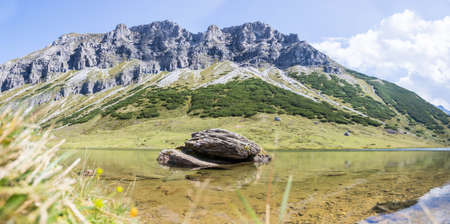 Lake with clear water in the foreground, rugged mountains in the backgroundの写真素材