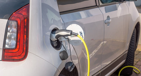 A white electric car is charged with power cable on the street