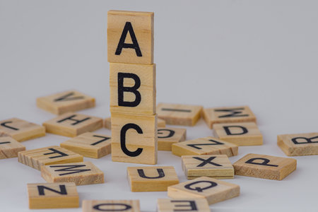 stack of square wooden blocks with the letters ABC surrounded by square wooden letters on a white backgroundの写真素材