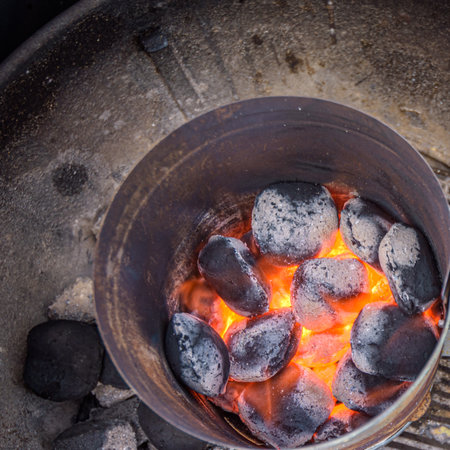 Top-down view of flaming hot charcoal briquettes igniting in a metal grill starter, ready for a barbecueの写真素材