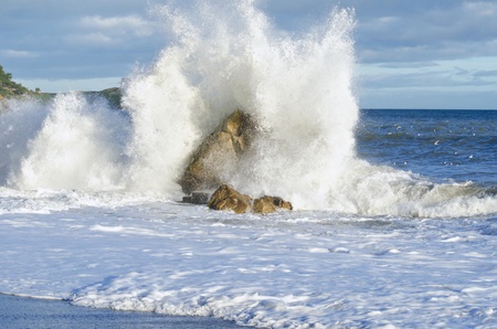 Wave crashing against rock is illuminated by sun の写真素材