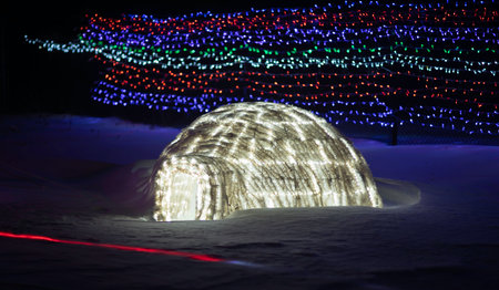 Illuminated igloo in the snow with Christmas lights in the backgroundの写真素材