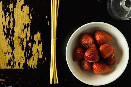 A glass jar, incense sticks  and a bowl of strawberries are arranged on a scratchy wooden surfaceの写真素材