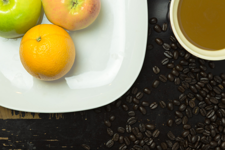 A plate with apples and oranges, a coffee mug and coffee beans on a scratchy. old wooden surfaceの写真素材