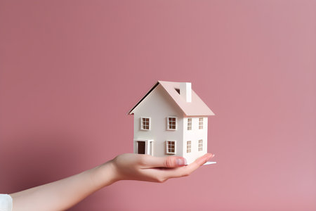 Female hand holding a model of a house on a pink background. real estate conceptの素材
