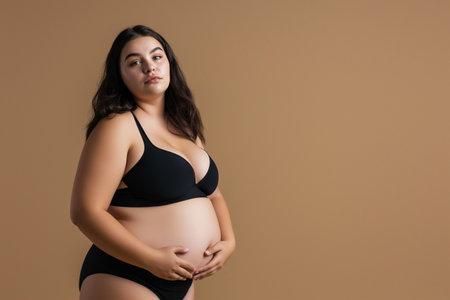 Pregnant woman in black underwear with big belly on beige backgroundの素材