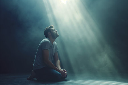 Young man sitting on the floor in a dark room with rays of lightの素材
