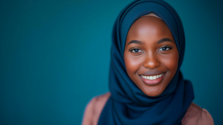 Portrait of beautiful african muslim woman wearing hijab against blue backgroundの素材