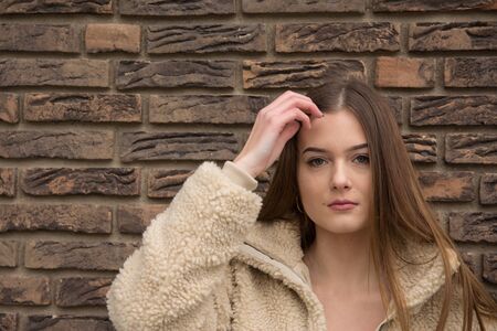 Young girl portrait with winter coat next to brick wallの写真素材