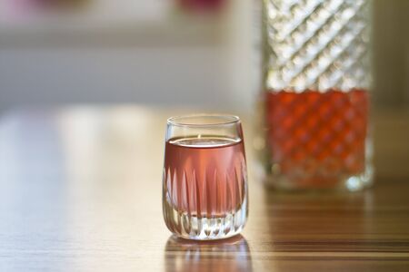 Pink colored liqueur in a crystal shot glass on wooden table. Bootle at the background.Soft and selective focus.の写真素材