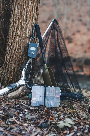 Fishing equipment box, scale, landing net lying on ground next to river and treeの写真素材