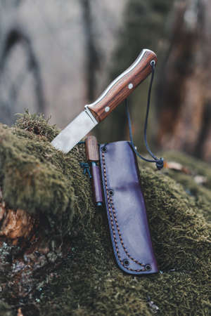 Outdoor knife stuck in the moss with leather case and tinderbox with blur background verticalの写真素材