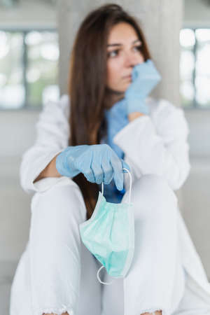 Sad and hopeless young female doctor holding protective mask for protecting from virus desease sitting on floor at hospital.の写真素材