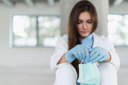 Sad and hopeless young female doctor holding protective mask for protecting from virus desease sitting on floor at hospital.の写真素材
