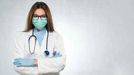 Female young doctor folded hands with protection medical mask, stethoscope over neck and white coat. Covid 19, coronavirus, healthcare concept banner.の写真素材