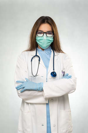 Female young doctor folded hands with protection medical mask, stethoscope over neck and white coat. Covid 19, coronavirus, healthcare concept banner.の写真素材