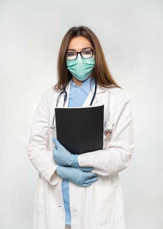 Female young doctor holding documents with protection medical mask, stethoscope over neck and white coat. Covid 19, coronavirus, healthcare concept banner.の写真素材