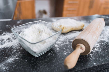White flour in glass bowl, wooden roller and dough in the kitchen ready for rolling.の写真素材