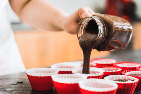 Housewife pours chocolate dough into baking molds for cupcakes. Close up.の写真素材