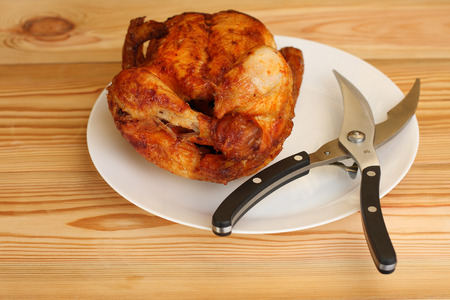whole grilled chicken with  shears for poultry on white plate on wooden tableの写真素材